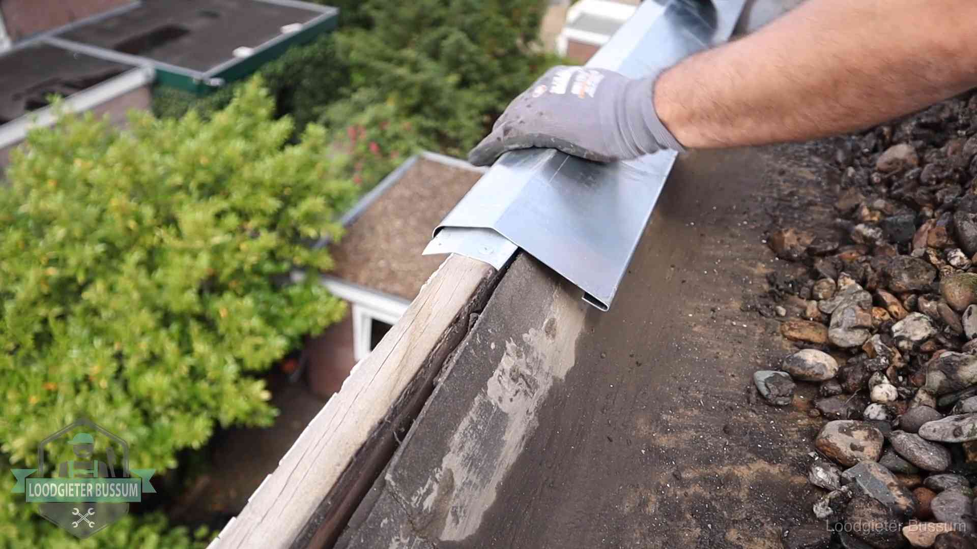Daklekkage per wijk in Bussum Dakdekker plaatst een zinken deklijst op een dakrand met uitzicht over een woonwijk in Bussum
