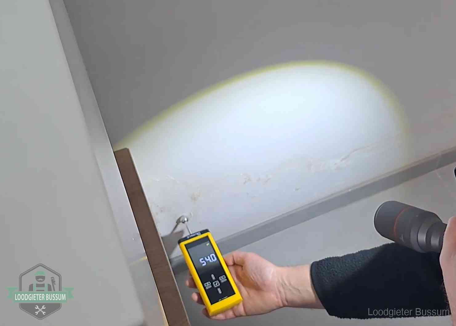 Vochtmeter tegen een natte wand met lekkagesporen in Bussum