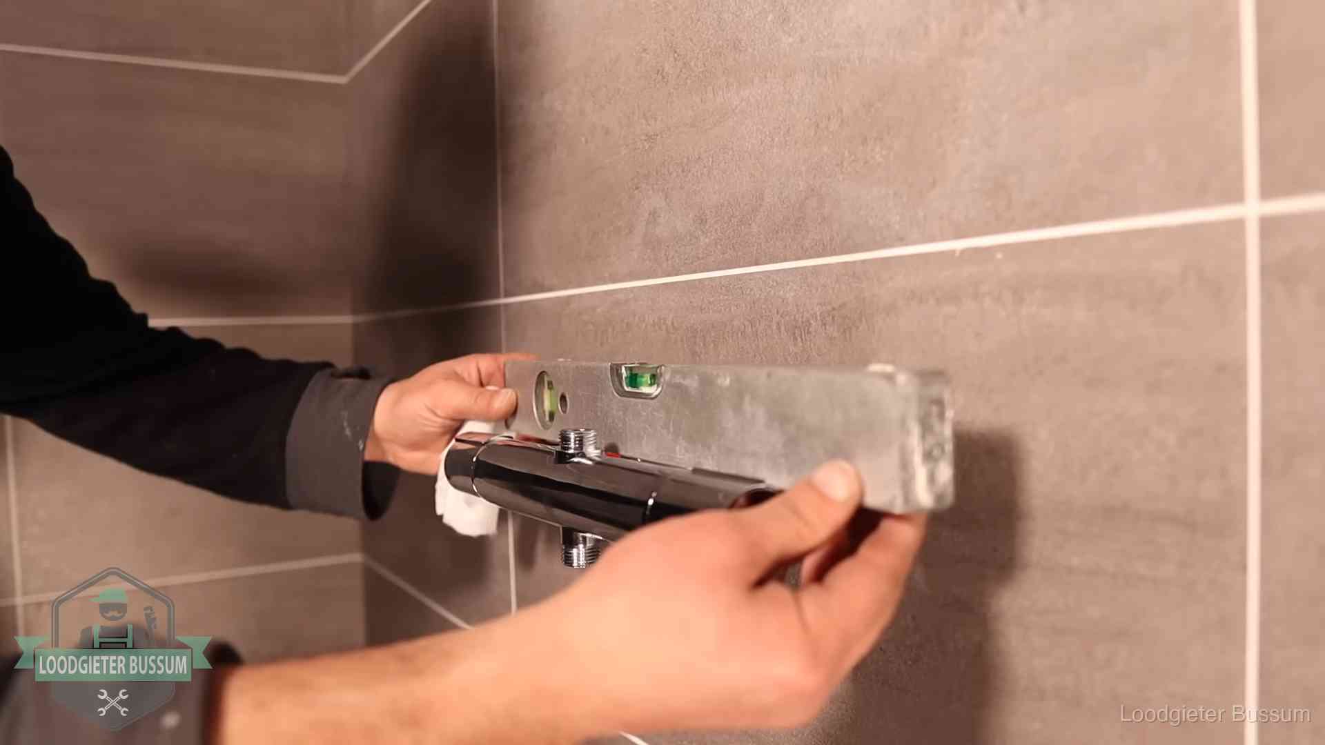 Loodgieter lijnt een douchekraan uit met een waterpas in een woning in Bussum