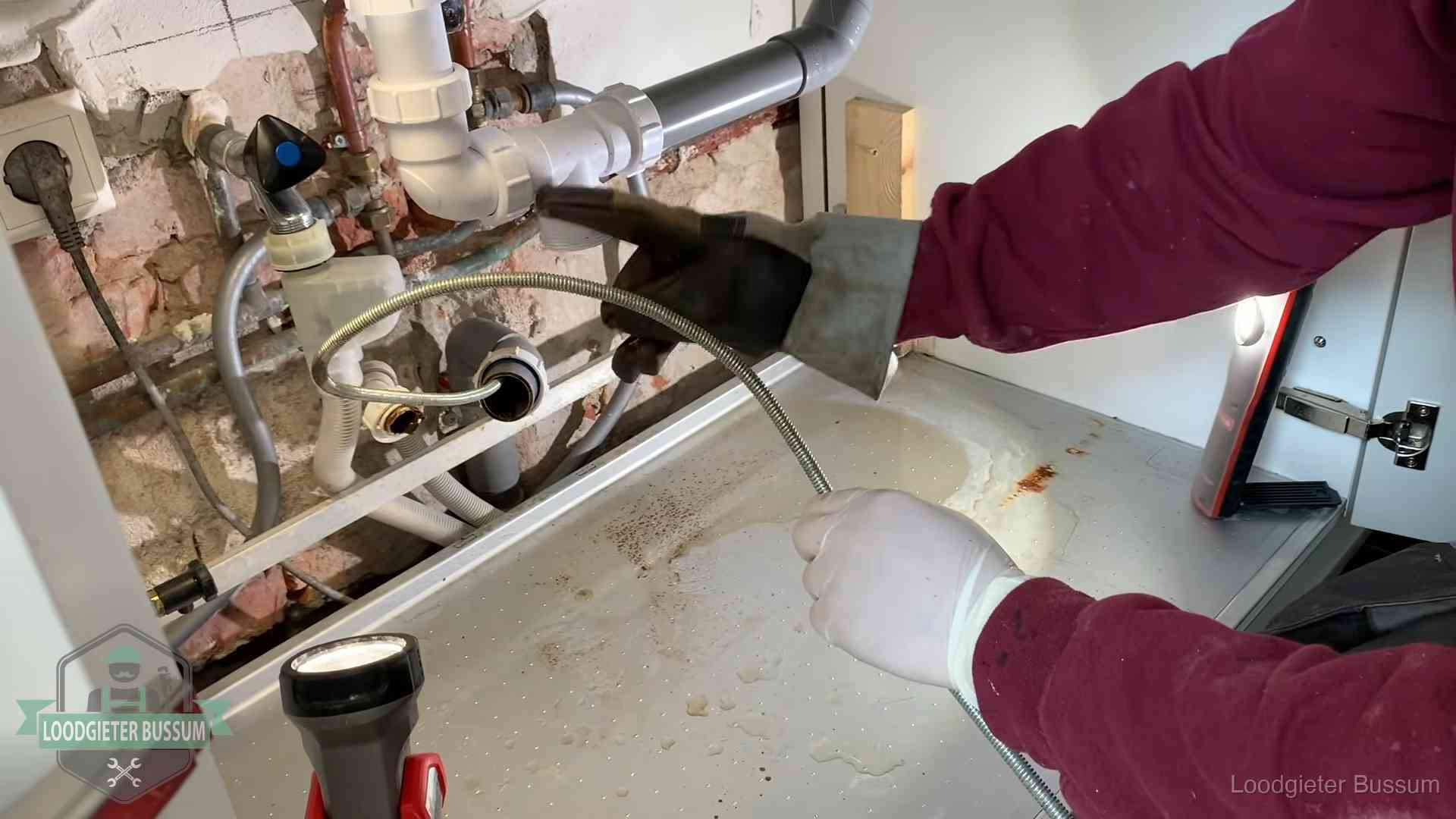 Ontstoppingsveer gaat in een geopende sifonaansluiting onder het aanrecht in Bussum