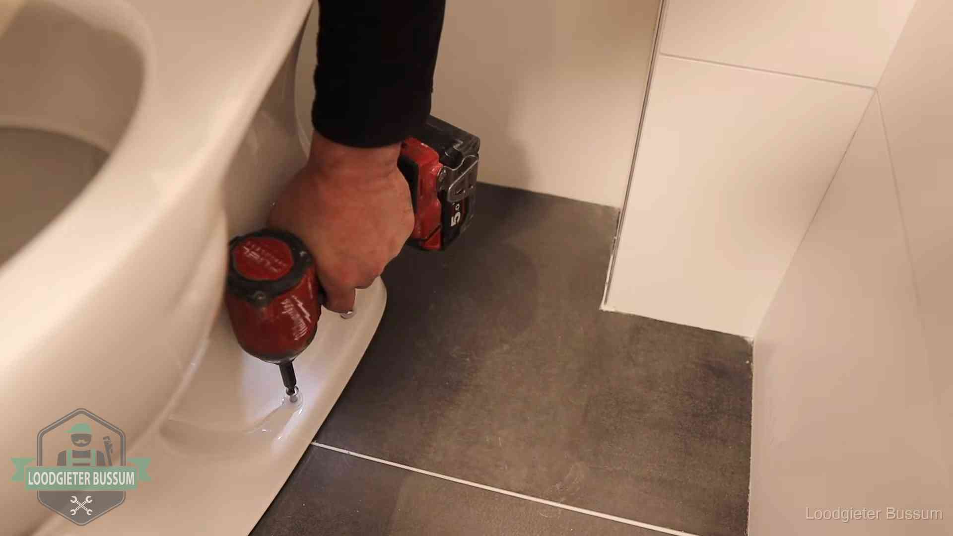 Loodgieter zet de voet van een wc-pot vast op de tegelvloer in Bussum
